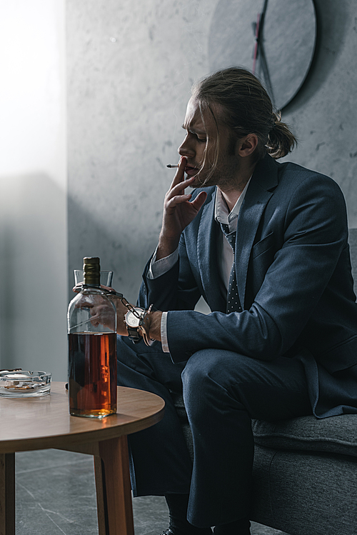alcohol addicted businessman with glass and bottle of whiskey smoking cigarette
