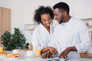 Young african american couple reading newspaper in kitchen