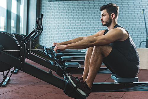 Young sportsman doing exercise on rowing machine in sports center