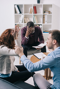 Frustrated african american psychiatrist with textbook and divorcing couple in office