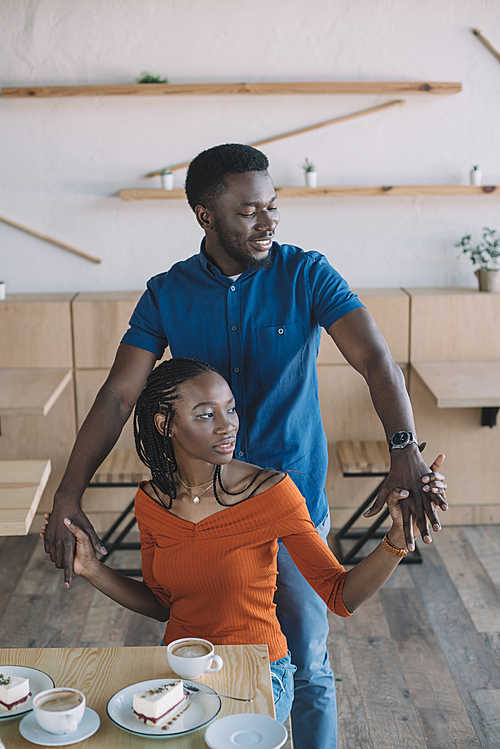 smiling african american couple holding hands on romantic date in coffee shop