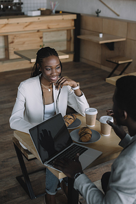 smiling african american friends sitting at table with laptop in coffee shop