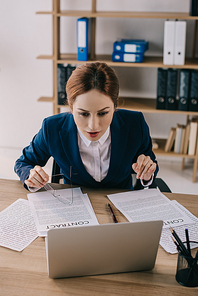 portrait of businesswoman in suit looking at laptop screen at workplace in office