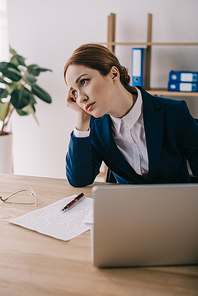 portrait of tired businesswoman looking away at workplace with laptop in office