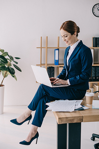 businesswoman working on laptop while sitting on table in office