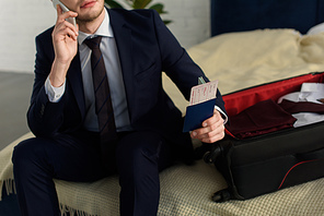 cropped view of businessman holding air ticket with passport while talking on smartphone