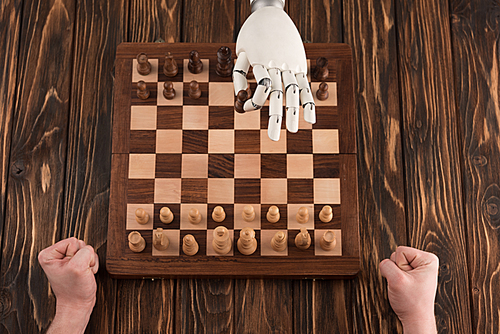 cropped shot of robot playing chess with human on wooden surface