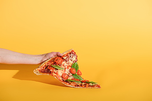 partial view of woman holding piece of pizza with cherry tomatoes in hand on yellow background