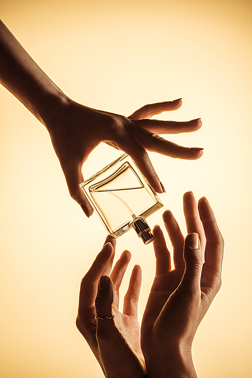 cropped view of women holding luxury perfume bottle, isolated on yellow