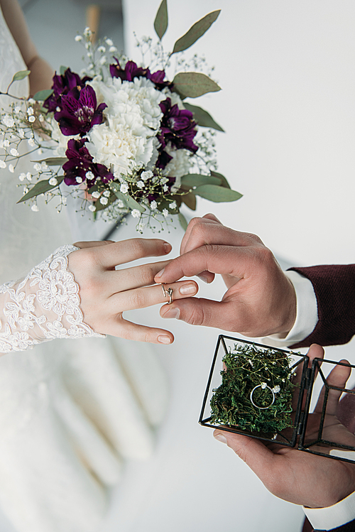 partial view of groom wearing wedding ring on bridal finger