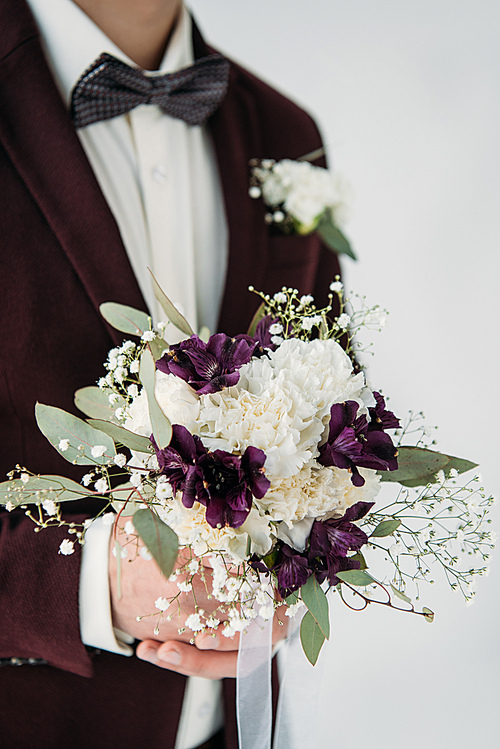 partial view of groom in suit with beautiful wedding bouquet in hands