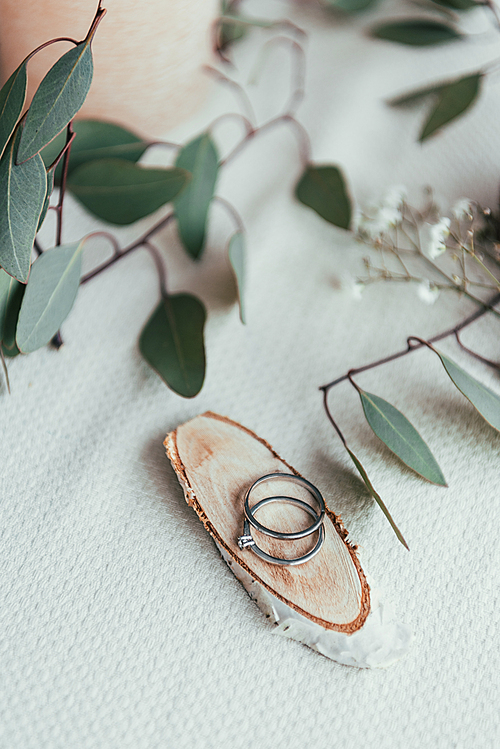 close up view of wedding rings on wooden decorative board and eucalyptus on tabletop