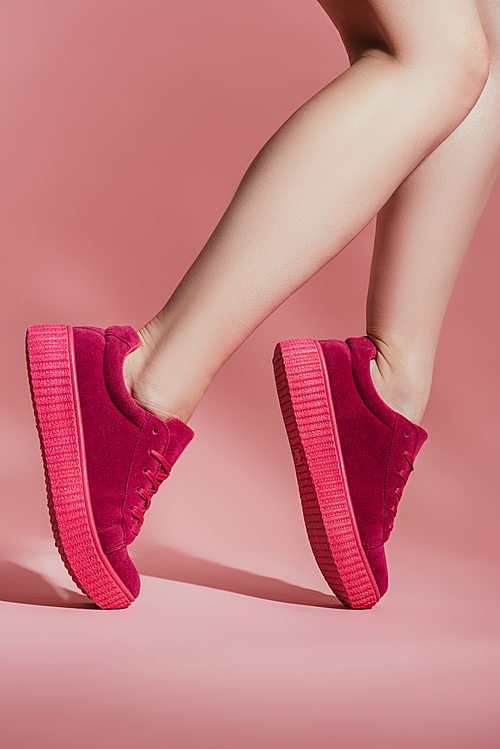 cropped shot of girl in stylish sneakers standing on toes on pink background