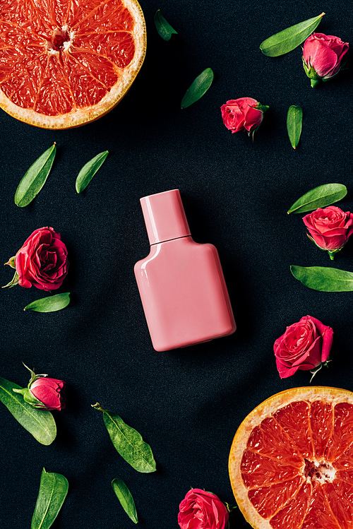 top view of bottle of perfume with rose buds and grapefruit slices around on black