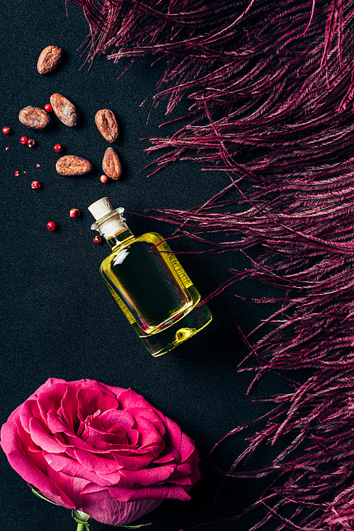 top view of bottle of perfume with red feather and rose bud on black