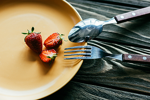 Fork and spoon on plate with strawberries on wooden table