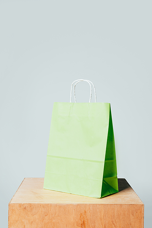 one light green paper bag on wooden stand isolated on white, summer sale concept
