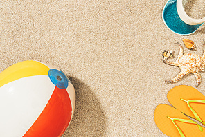 top view of arrangement of colorful beach ball, flip flops and cap on sand