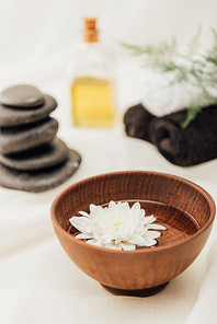 selective focus of arrangement of spa treatment accessories and chrysanthemum flower in wooden bowl on white background