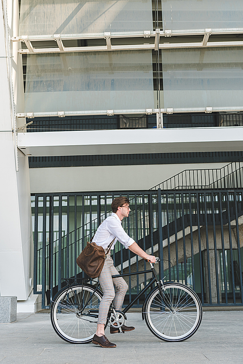 side view of stylish young man riding vintage bicycle on city street