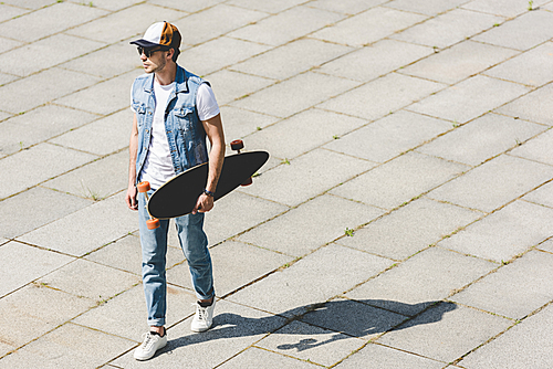 high angle view of handsome young man walking with skateboard in hand