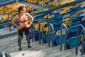 high angle view of sportive young woman standing on stairs at sports stadium with arms akimbo