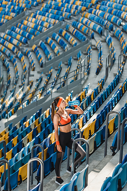 high angle view of beautiful young woman drinking water while standing on stairs at sports stadium