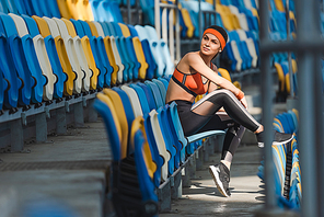 side view of beautiful young woman sitting on tribunes at sports stadium