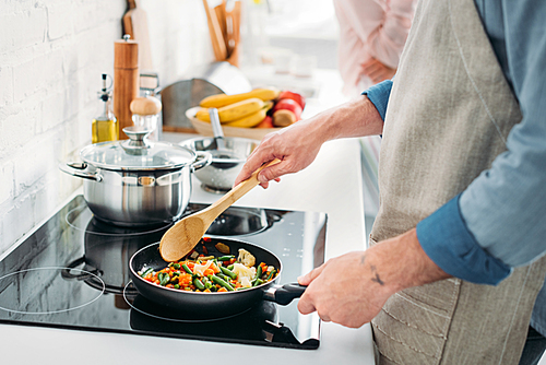 cropped image of boyfriend frying vegetables on frying pan in kitchen