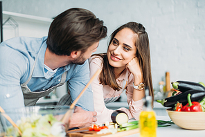 smiling couple looking at each other while cooking in kitchen