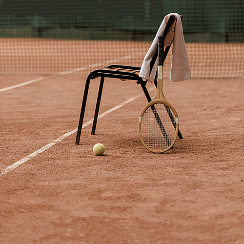 chair with towel and tennis racket with tennis ball at court