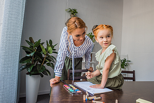 mother and adorable daughter drawing in album while sitting on table