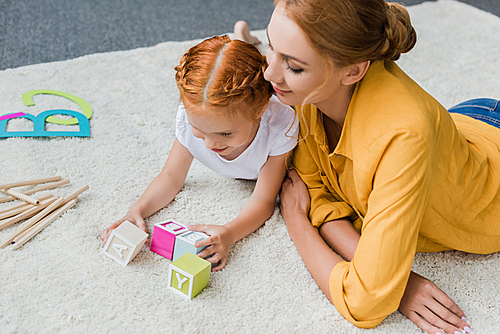 mother and daughter playing with letter cubes on floor at home