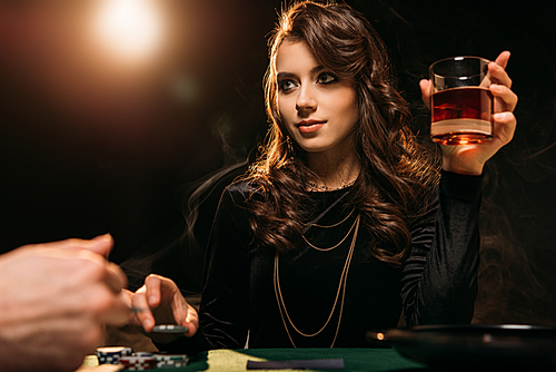 low angle view of attractive girl holding glass of whiskey at poker table in casino