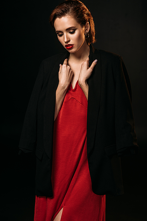attractive girl in red dress and black jacket looking down isolated on black