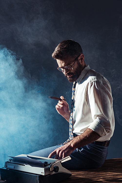 handsome smoking man sitting on table with typewriter