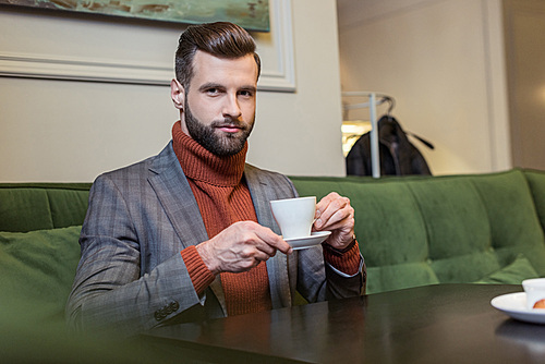 handsome man in formal wear , sitting at table and drinking coffee in restaurant