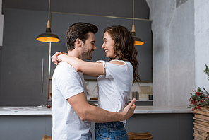 smiling couple looking at each other and hugging in kitchen