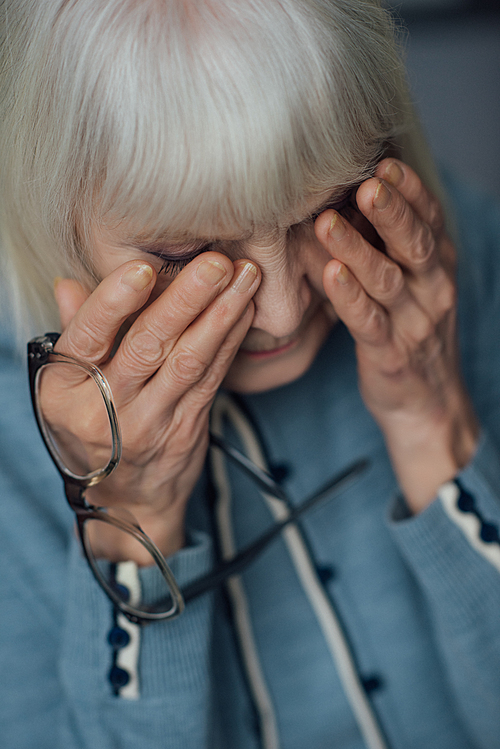 selective focus of senior woman with glasses and grey hair wiping tears and crying at home