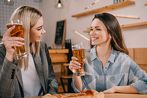 attractive friends smiling while holding glasses of beer in bar