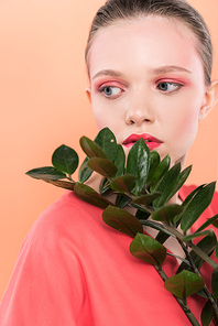 beautiful stylish girl looking away and posing with plant isolated on living coral