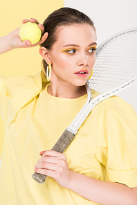 beautiful stylish girl holding tennis racket and ball while posing with limelight on background