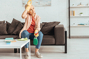 Tired woman with cleaning spray sitting on sofa