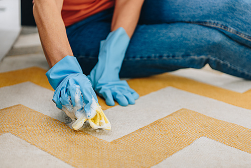 Cropped view of woman in blue rubber gloves cleaning carpet