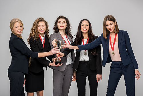 successful businesswomen holding trophy smiling isolated on grey