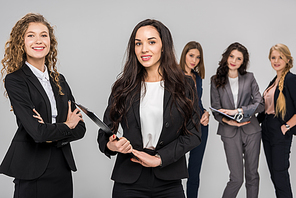 selective focus of cheerful businesswoman holding clipboard near colleague with attractive coworkers standing on background