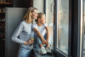 portrait of mother and daughter looking out window together at home