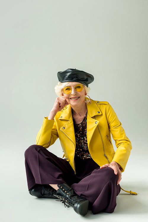 stylish senior lady in yellow jacket and leather beret, isolated on grey