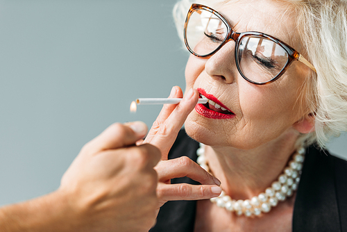 senior woman with pearl necklace smoking cigarette, isolated on grey
