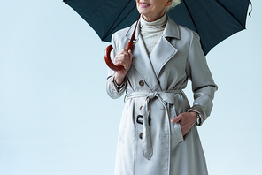 cropped view of senior lady in trench coat holding umbrella, isolated on grey